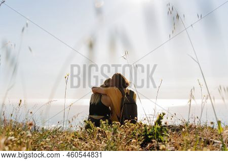 Rear View Of Romantic Young Couple Looking At Scenic Seascape Against Clear Sky While Sitting On Mou