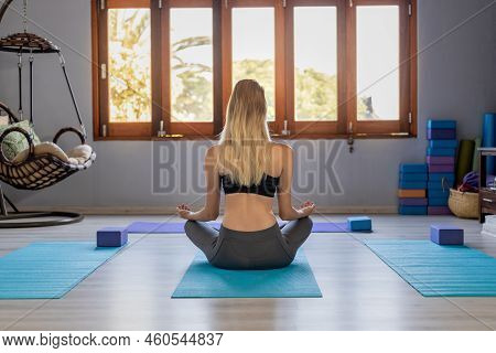 Rear View Of Caucasian Young Woman With Blond Hair Meditating While Sitting On Exercise Mat In Yoga 