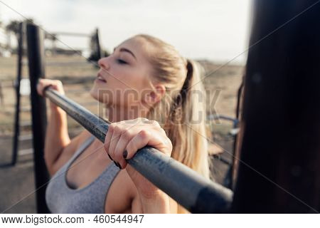 Confident Athletic Young Woman With Blond Hair Practicing Pull Up Exercise On Rod Against Clear Sky
