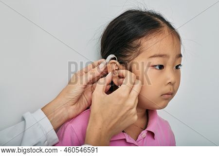 Asian Little Girl While Installing Bte Hearing Aid By Audiologist, Close-up. Hearing Solutions For C