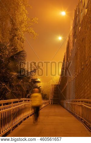 Run Along The Night Street In The Light Of Lanterns. A Human Figure Runs Along A Path. Long Exposure