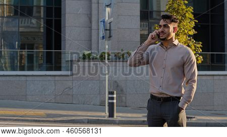 Hispanic Business Man Arabic Guy Stands On Street Background Of City Buildings Talking On Mobile Pho