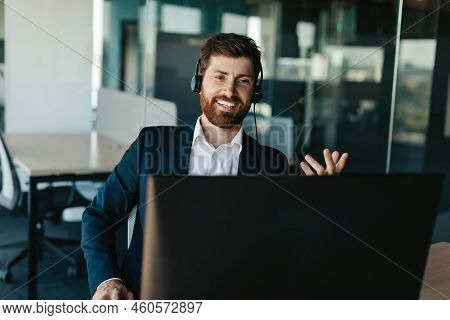Positive Entrepreneur With Beard In Suit Wearing Headphones And Gesticulating At Computer Webcamera 