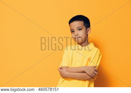 A Little Boy Of Preschool Age Is Standing On An Orange Background In A Yellow Shirt, Looking Thought