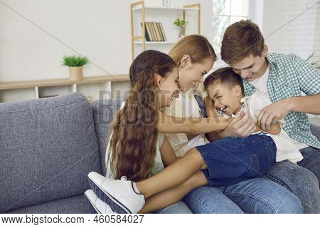 Cheerful Family With Children Having Fun Together And Fooling Around Tickling On Sofa In Living Room