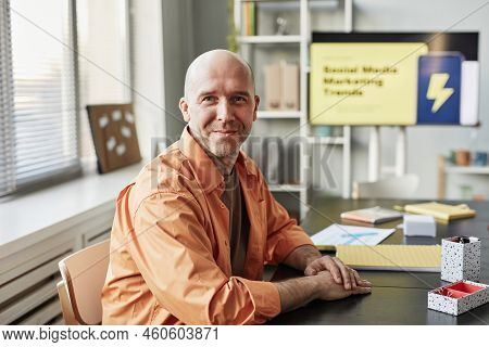 Portrait Of Smiling Bald Man Looking At Camera While Sitting At Workplace In Casual Office Setting