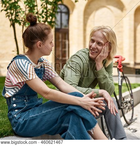 Young Caucasian Couple Sitting And Looking At Each Other Near Their Bicycles On City Square. Modern 