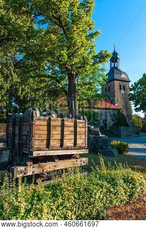 Wooden Mine Transport Cart Of The Former Mine In Flechtingen, In The Background The Evangelical Chur