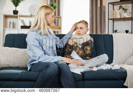 Pleasant 40-aged Caucasian Mother Measuring Temperature Of Her Teen Boy, Which Is Sitting Near Her O