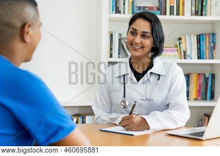 Laughing Hispanic Female Doctor  Talking With Healthy Patient At Hospital