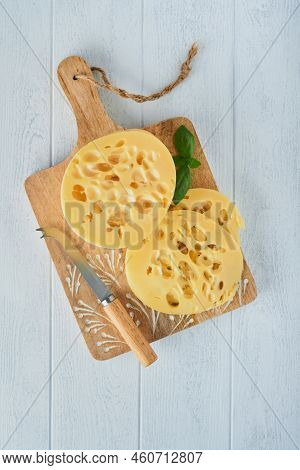 Cheese Maasdam Or Radamer. Piece Of Cheese On Wooden Stand Board On White Wooden Table Background. T