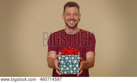 Positive Smiling Bearded Handsome Young Man Presenting Birthday Gift Box Stretches Out Hands, Offer 