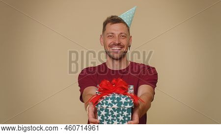 Positive Smiling Bearded Handsome Young Man Presenting Birthday Gift Box Stretches Out Hands, Offer 