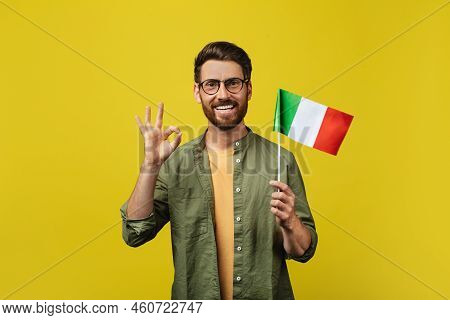 Positive Man Showing Flag Of Italy And Gesturing Okey, Posing Over Yellow Studio Background And Smil