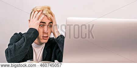 Young Office Worker Is Shocked And Surprised Looking At A Laptop Clutching His Head, Sitting At A De
