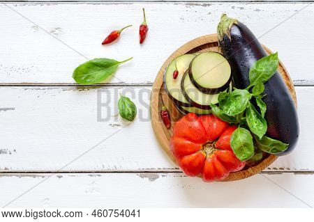 Eggplant, Tomato And Basil, Top View. Fresh Vegetables And Herbs On A Wooden Plate.