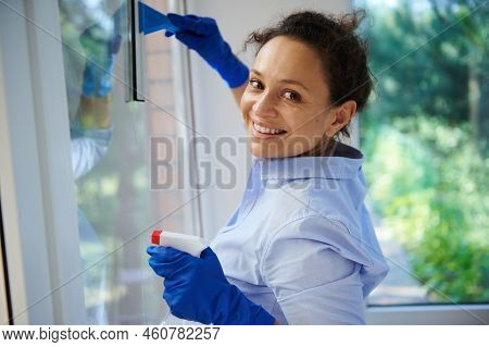 Close-up Portrait Of Beautiful Multi-ethnic Woman Smiling At Camera, Washing And Wiping Window With 