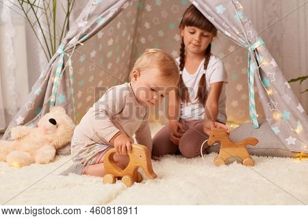 Horizontal Shot Of Charming Sibling Girls Playing Together In Peetee Tent With Wooden Eco Toys, Todd
