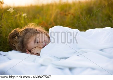 The Girl Sleeps On White Bed Linen In Nature In The Grass, In The Fresh Air. Protection From Mosquit