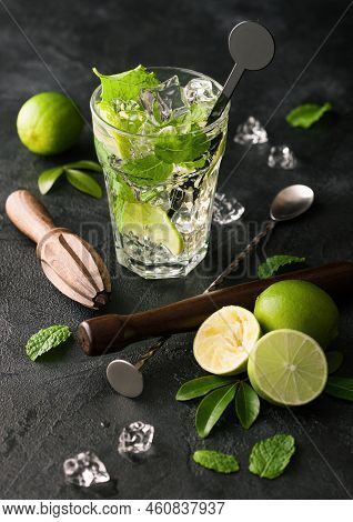 Glass Of Mojito Cocktail With Ice Cubes Mint And Lime On Black Board With Spoon And Muddler And Fres