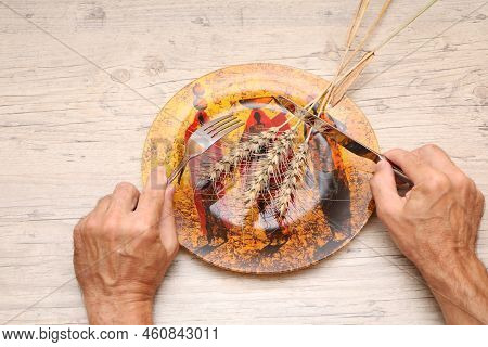 On A Plate With African Patterns Is A Grain Ear, In The Hands Of A Fork And A Knife. A Symbol Of Hun