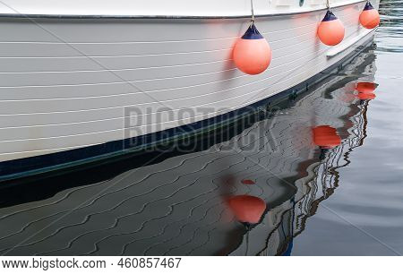Three Bright Orange Buoys Hanging On Side Of Boat Reflected In Calm Water,