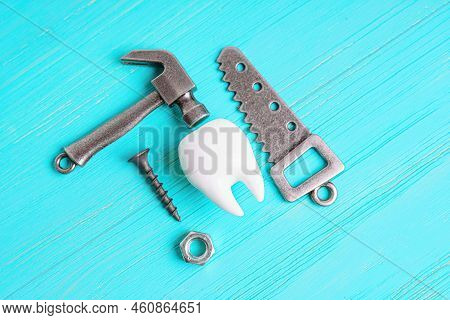 Human Tooth Model, Steel Hammer, Wrench, Handsaw, Screw And Nut Isolated On A Blue Wooden Background