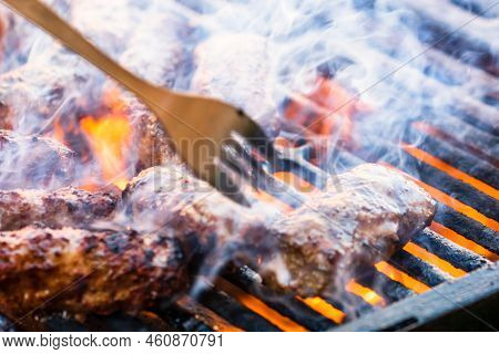Preparing Meat Rolls Called Mici Or Mititei On Barbecue. Close Up Of Grill With Burning Fire With Fl