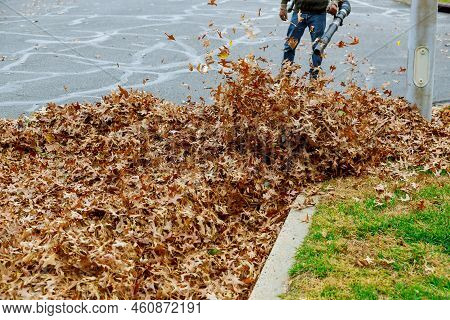 A Municipal Worker Cleans Fallen Leaves Near Houses During The Autumn Season An Uzing Blower