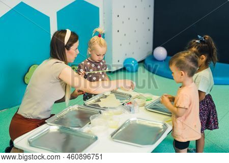 Sensory Play At Multi-cultural Nursery School. Toddlers With Their Teacher Playing With Striped Stra
