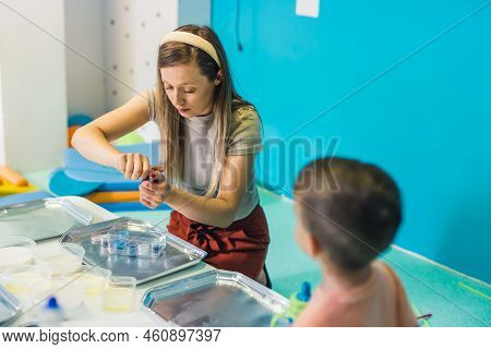 Sensory Play At Multi-cultural Nursery School. Toddlers With Their Teacher Playing With Striped Stra