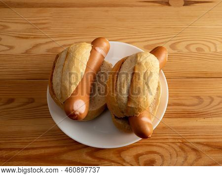 Boiled Sausage With A Bun On A Wooden Background.