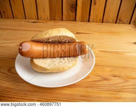 Boiled Sausage With A Bun On A Wooden Background.