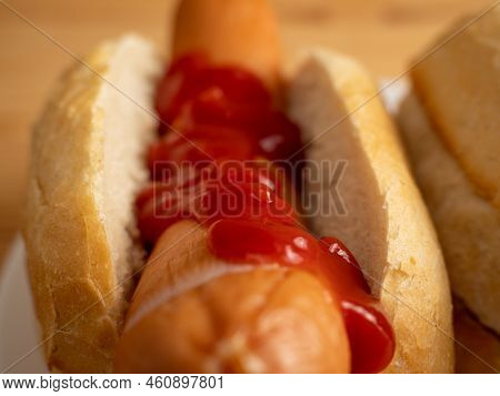 Boiled Sausage With A Bun On A Wooden Background.