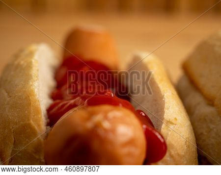 Boiled Sausage With A Bun On A Wooden Background.