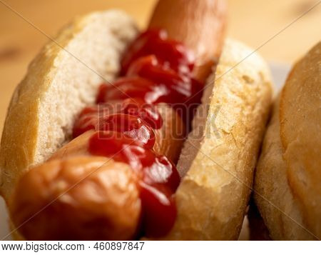 Boiled Sausage With A Bun On A Wooden Background.