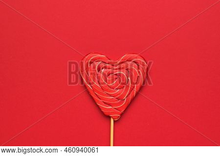 A Large Red Candy On A Stick In The Shape Of A Heart On A Red Background. Minimal Concept Of Sweet L