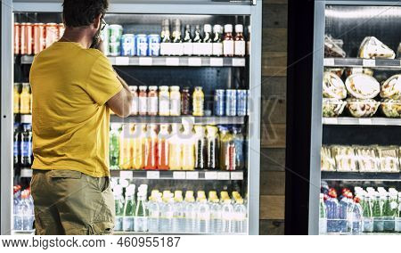 Man Alone And Isolated At The Supermarket Or Minimarket Choosing His Drink Or Snack In Big Fridge Wi