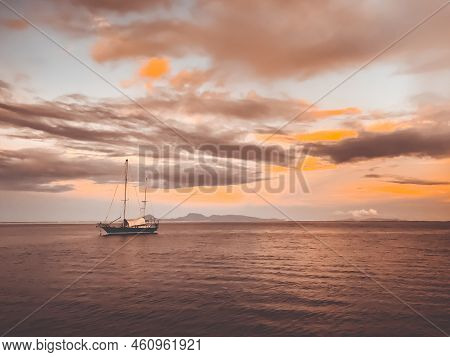 Bright Sunset Sea Landscape. Yacht Sailing Calm Ocean Water Under Vibrant Orange Sky. Impressive Col