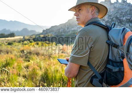Mature Male Hiker With Backpack Wearing Hat And Navigating Direction Over Smartphone While Enjoying 