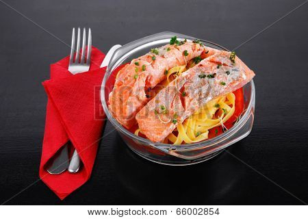 fresh fried natural pink salmon on italian traditional tagliatelle backed with tomato and vegetables served over black wooden table