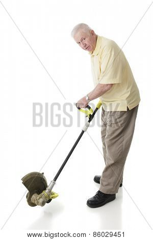 A senior adult man looking at the viewer while demonstrating how a weed whacker is used for edging.  On a white background.