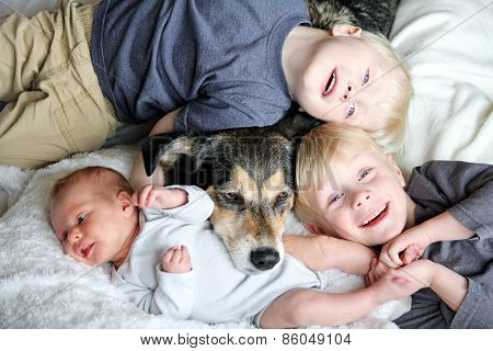 Three Happy Young Children Snuggling With Pet Dog In Bed