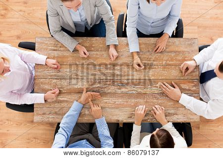 business, people and team work concept - close up of creative team sitting at table and pointing finger to something in office