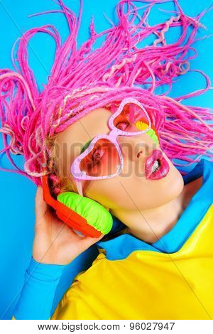 Ultra trendy DJ party girl in bright clothes, headphones and with bright dreadlocks. Disco, party. Show business. Bright fashion.