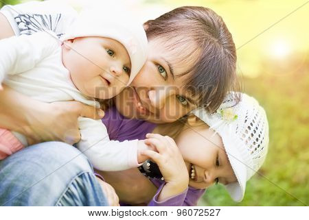 Young happy mother playing with two little children outside