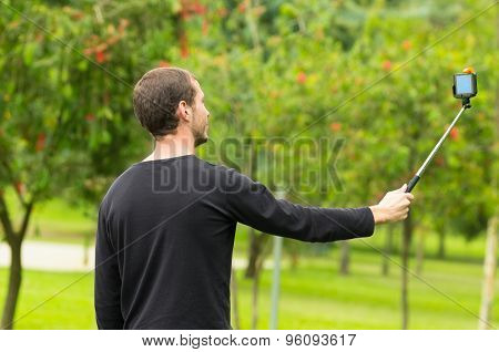 Hispanic man posing with selfie stick in park environment, shot from side profile angle