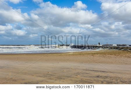 The New Jersey shore at manasquan Inlet. The ocean is rough as there is a storm out to sea. There is a lone person standing on a rock jetty.