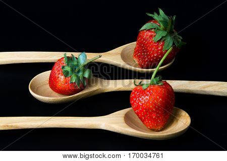 strawberry in wooden spoon on black background isolated