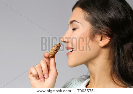 Pretty young woman eating tasty cookie, on grey background